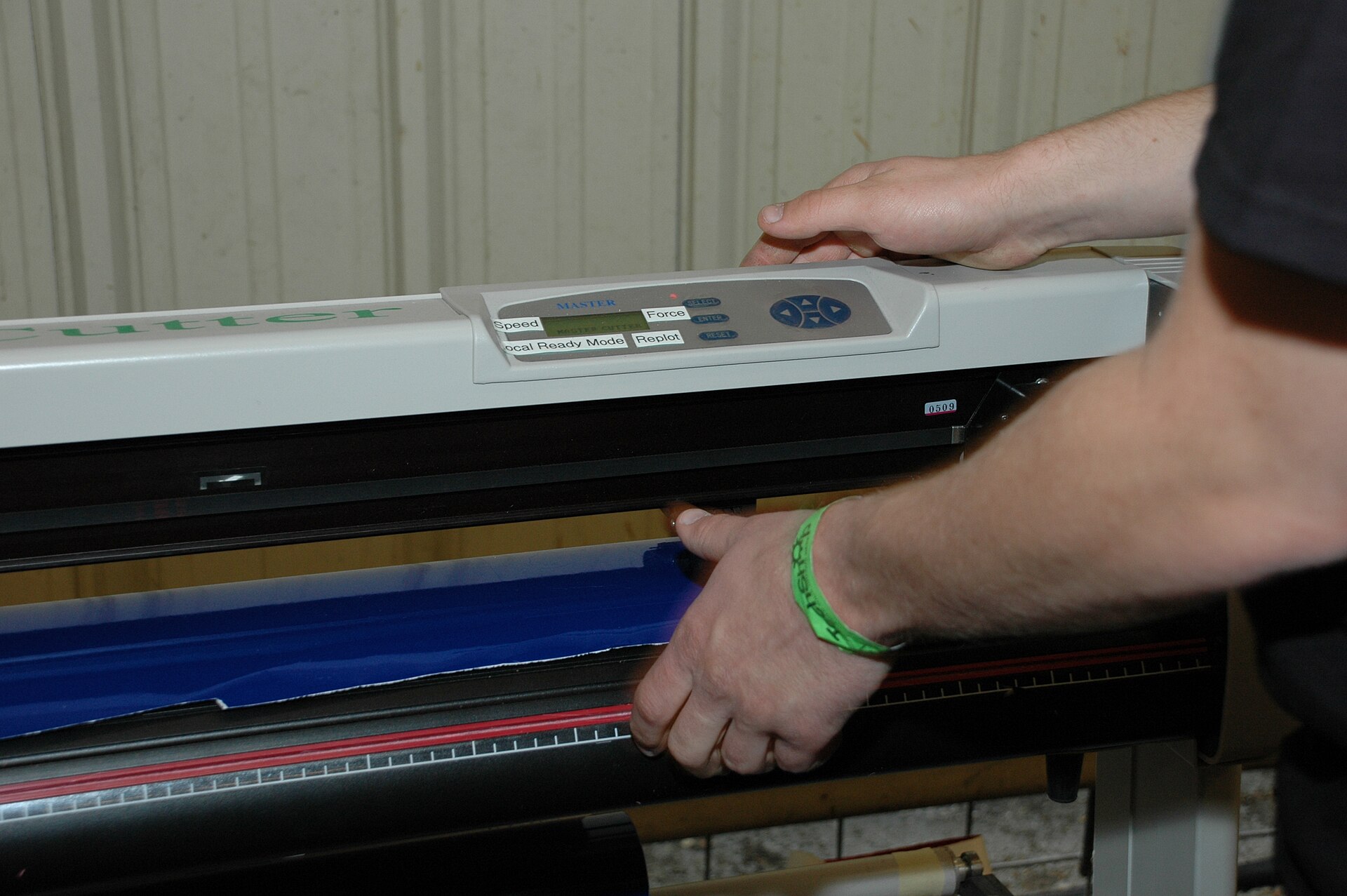 Manos cargando un rollo de vinil textil azul en una plotter de corte